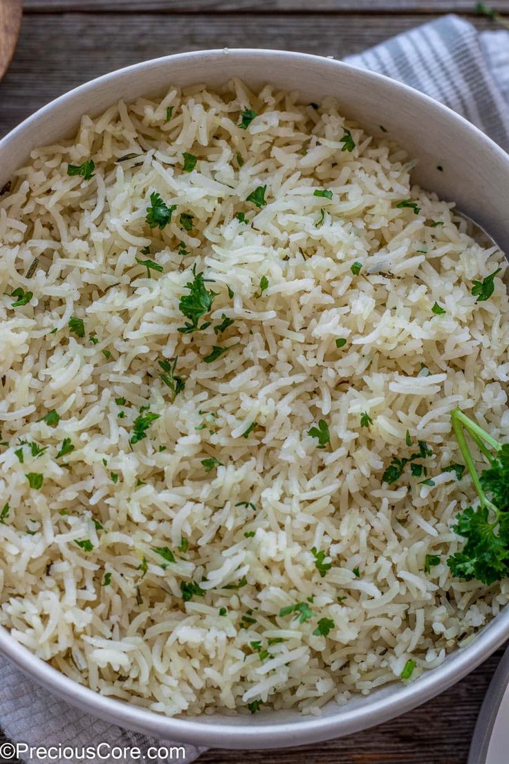 a white bowl filled with rice and parsley on top of a table next to utensils