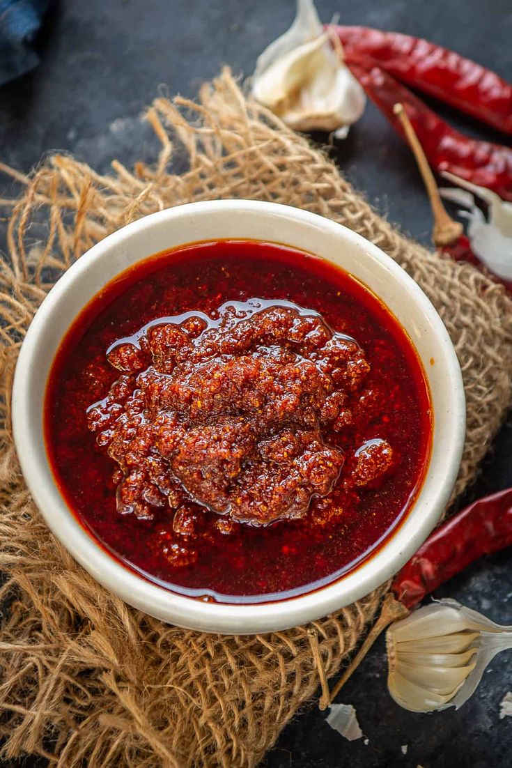 a white bowl filled with chili sauce next to garlic and red peppers on a table