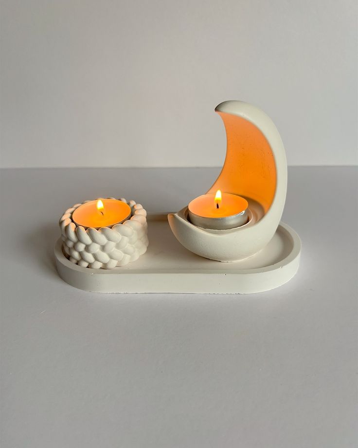 two candles sitting on top of a white plate next to a moon shaped candle holder