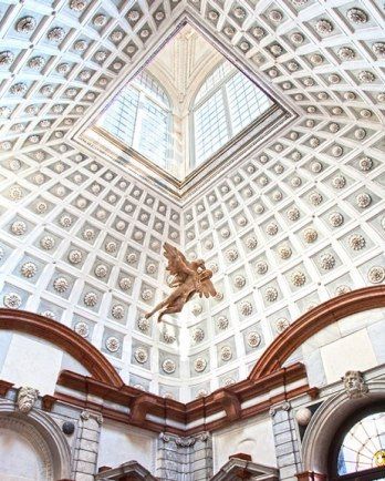 an ornate ceiling in a building with statues on the sides and windows above it,