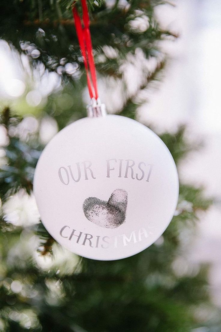 a white ornament hanging from a christmas tree with a handprint on it