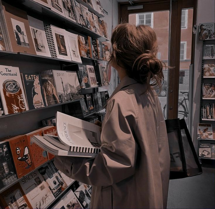 a woman is looking at books in a book store while holding an electronic device and reading them