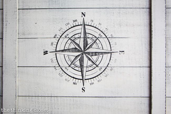 an old compass drawing on the side of a wooden wall with white paint and wood planks