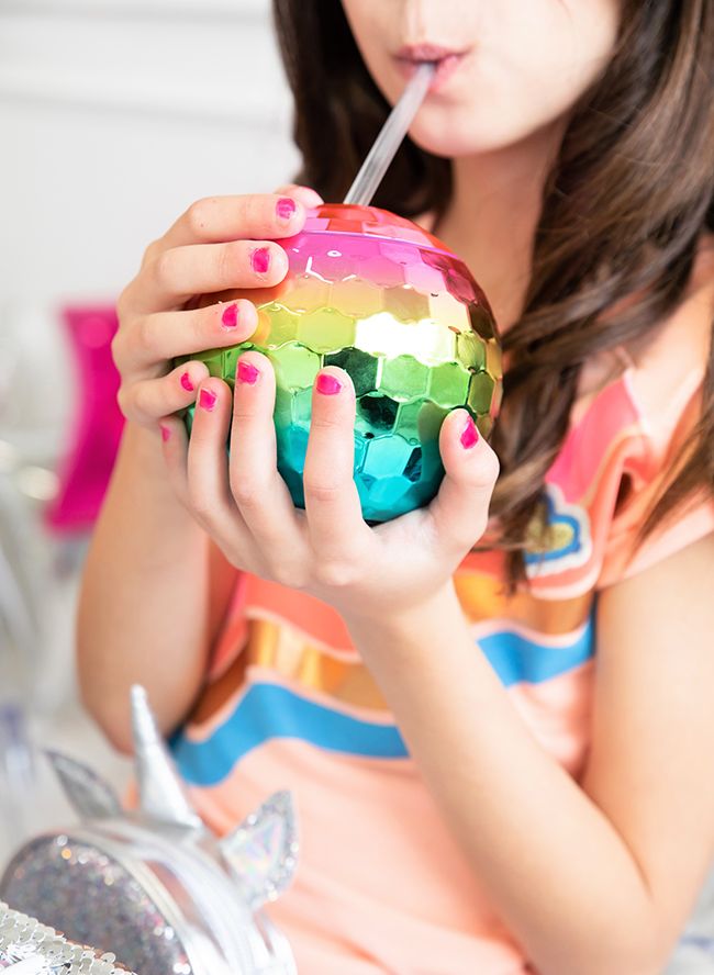 a young woman drinking from a straw in her hand while holding a colorful ball and toothbrush