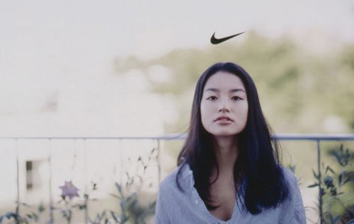 a woman standing in front of a fence with a nike logo above her head,