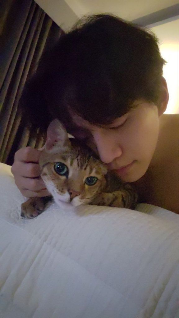 a woman is cuddling her cat on top of the bed while looking at the camera