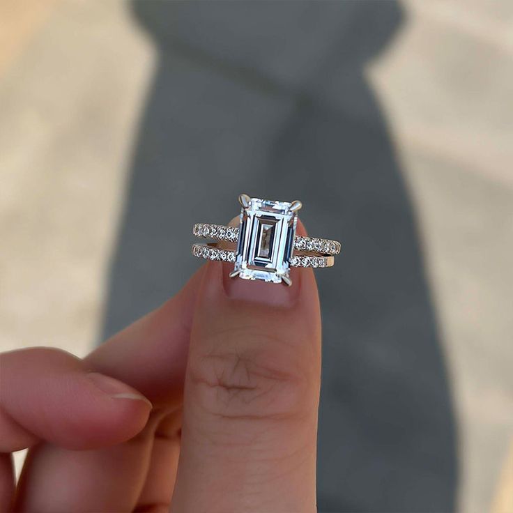 a person holding up a ring with an emerald stone in the middle and diamond band around it