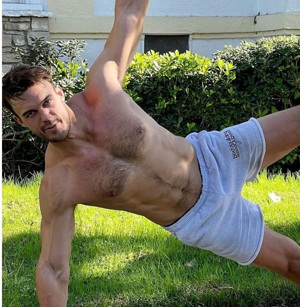 a shirtless man is doing yoga outside in the grass with his legs spread out