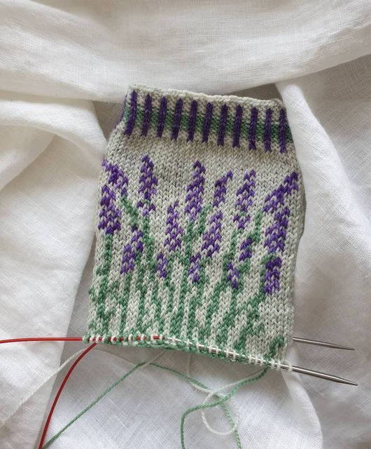 a close up of a knitted object on a white cloth with purple and green flowers