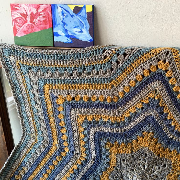 a crocheted blanket sitting on top of a wooden chair next to a painting