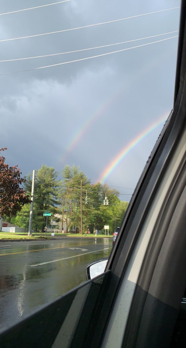 a rainbow is seen in the sky over a street with power lines and cars on it