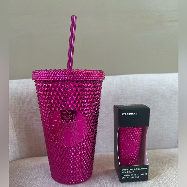 a pink tumbler next to a black box on a white couch with the lid open