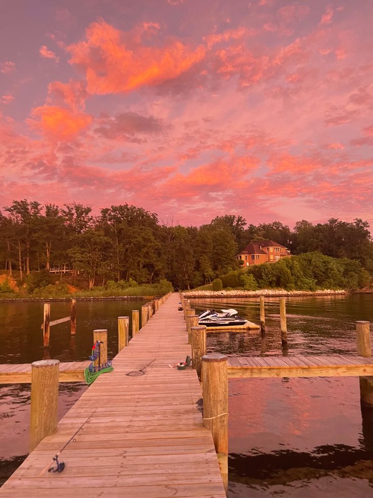 a dock that is next to the water with a boat on it and pink clouds in the sky