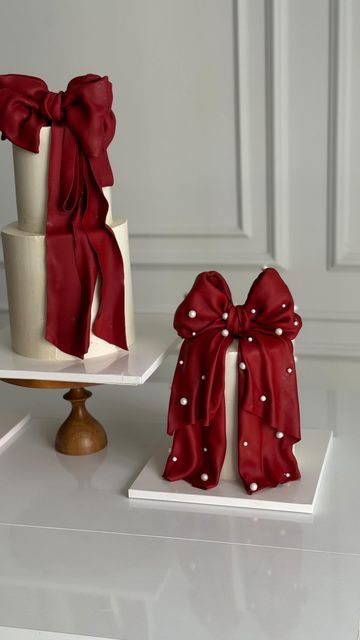 two cakes decorated with red bows and pearls on white trays next to each other