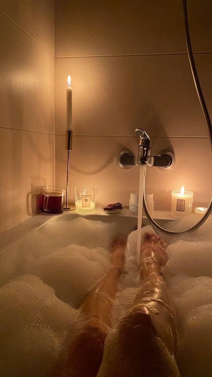 a person laying in a bathtub with candles on the side and water running down it