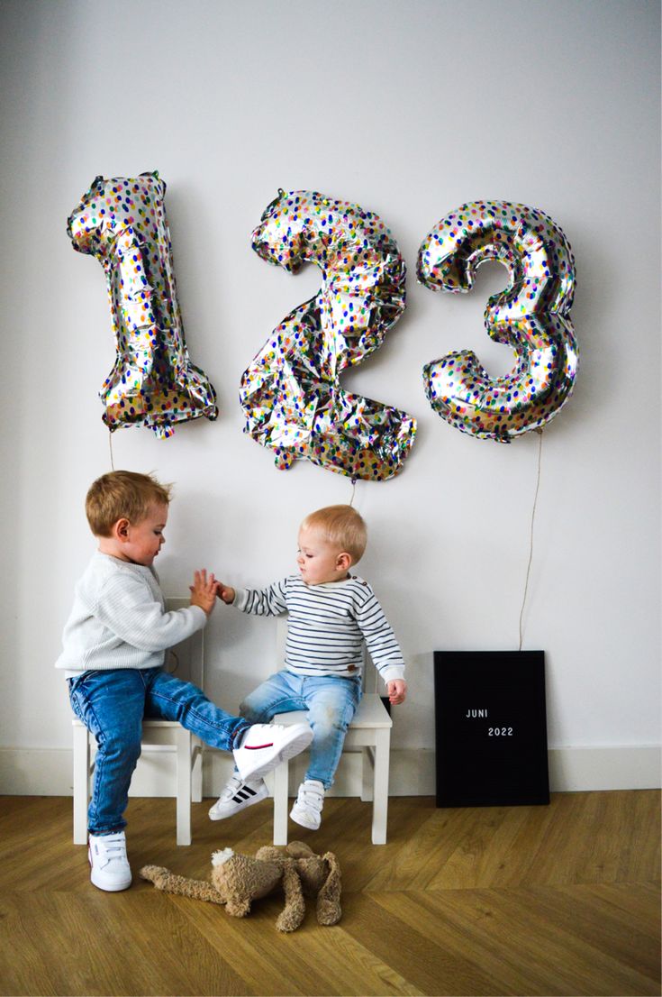 two young boys sitting on a bench in front of balloons that spell the number thirteen