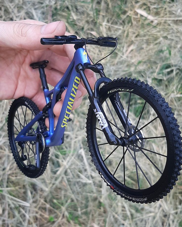 a hand holding a blue mountain bike on top of a grass covered field next to dry grass