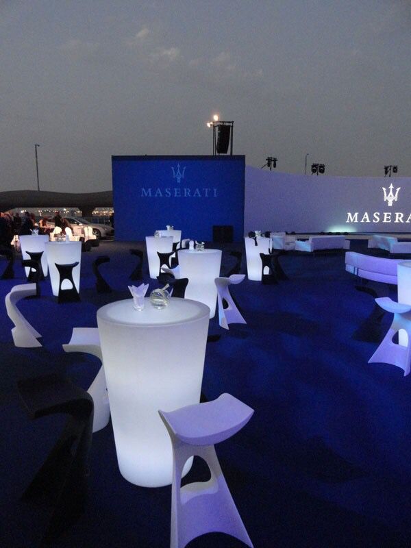 an outdoor event with white tables and chairs lit up at night, in front of a sign that reads maserati