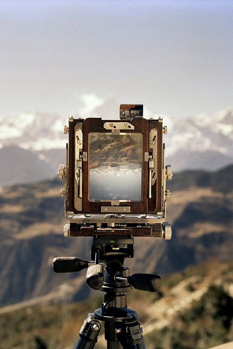 an old fashioned camera on top of a tripod in front of some mountains and snow capped peaks