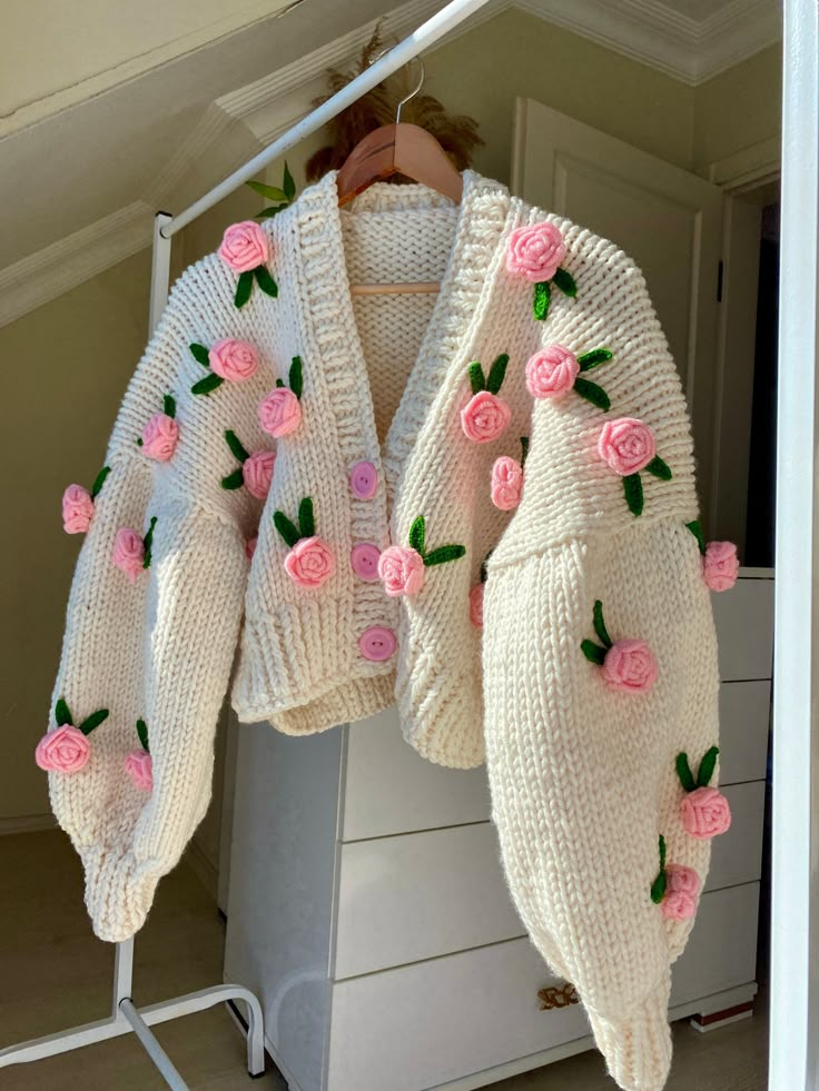 a white sweater with pink roses on it hanging from a clothes rack in a closet