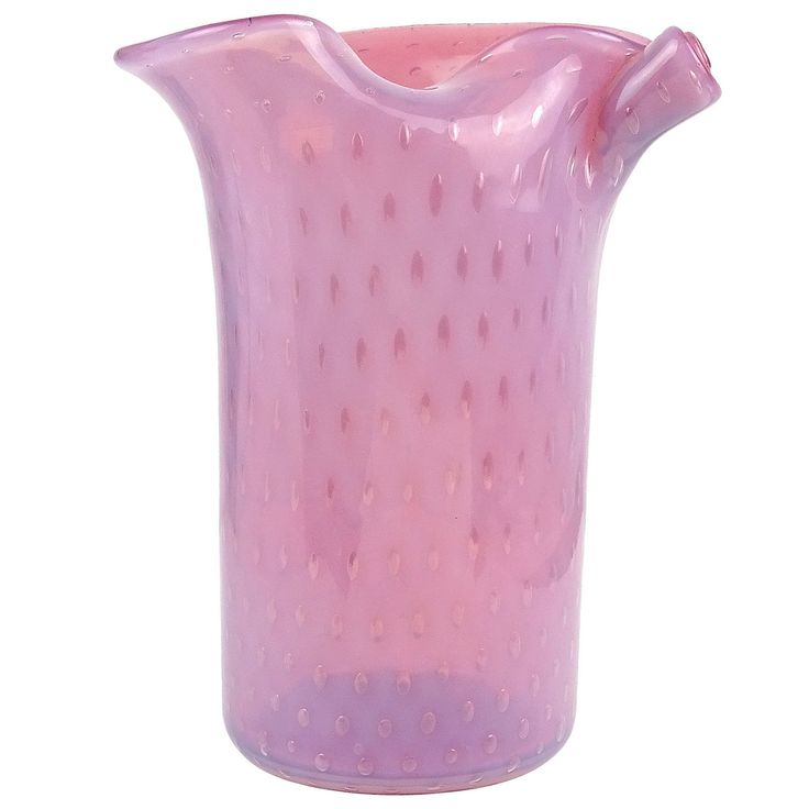 a pink glass vase with dots on the bottom and handle is shown in front of a white background