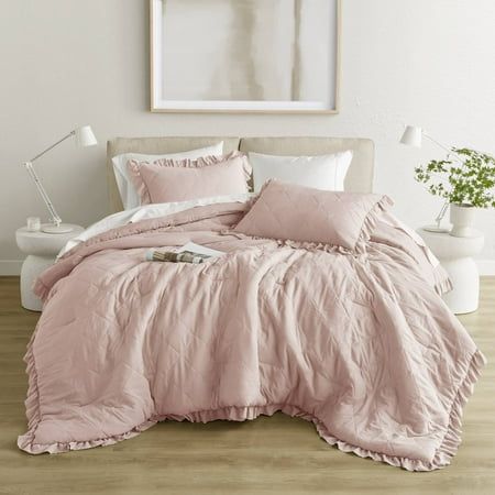 a bed with pink comforter and pillows in a white room next to a painting on the wall