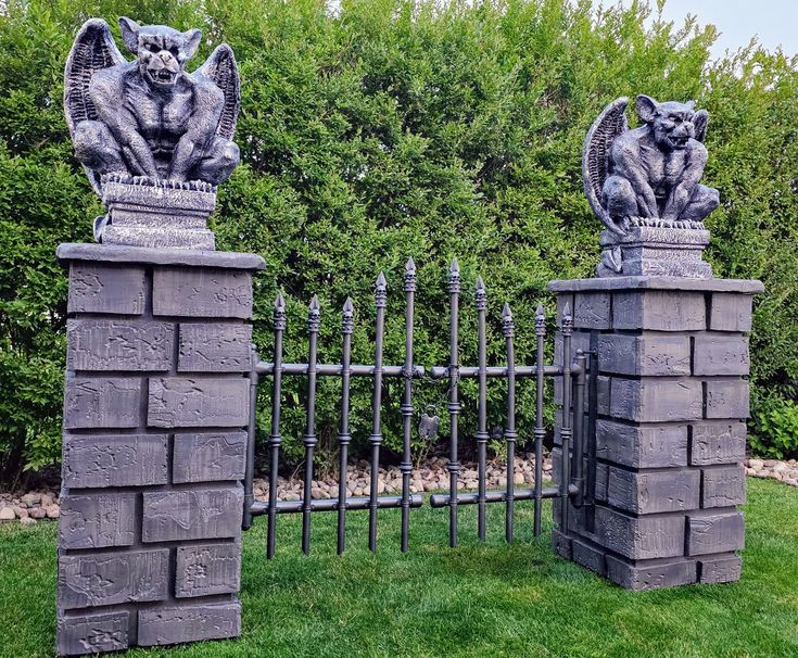 two gargoyle statues on top of stone pillars in front of a garden fence