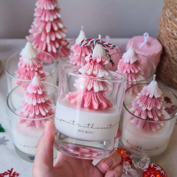 a person holding a glass filled with pink christmas trees on top of a white table