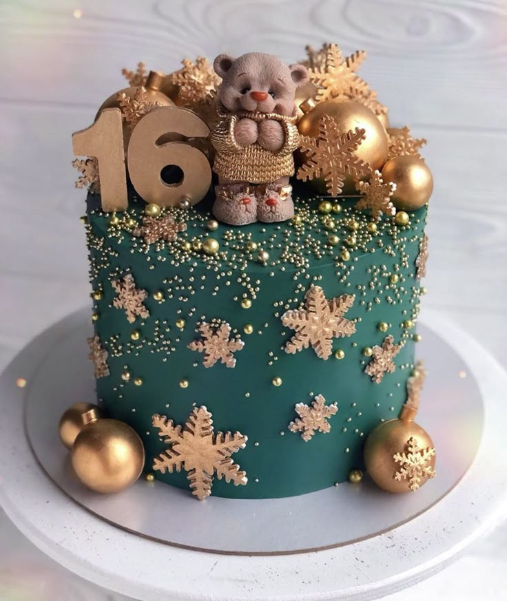 a green cake with gold snowflakes and a teddy bear sitting on the top