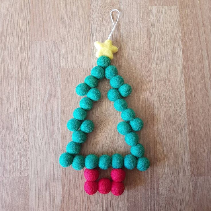 a felt christmas tree ornament hanging on a wooden table with a star and red pom - poms