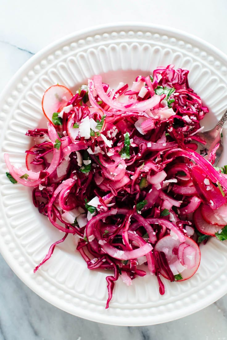 a white bowl filled with red cabbage salad on top of a marble countertop next to a fork