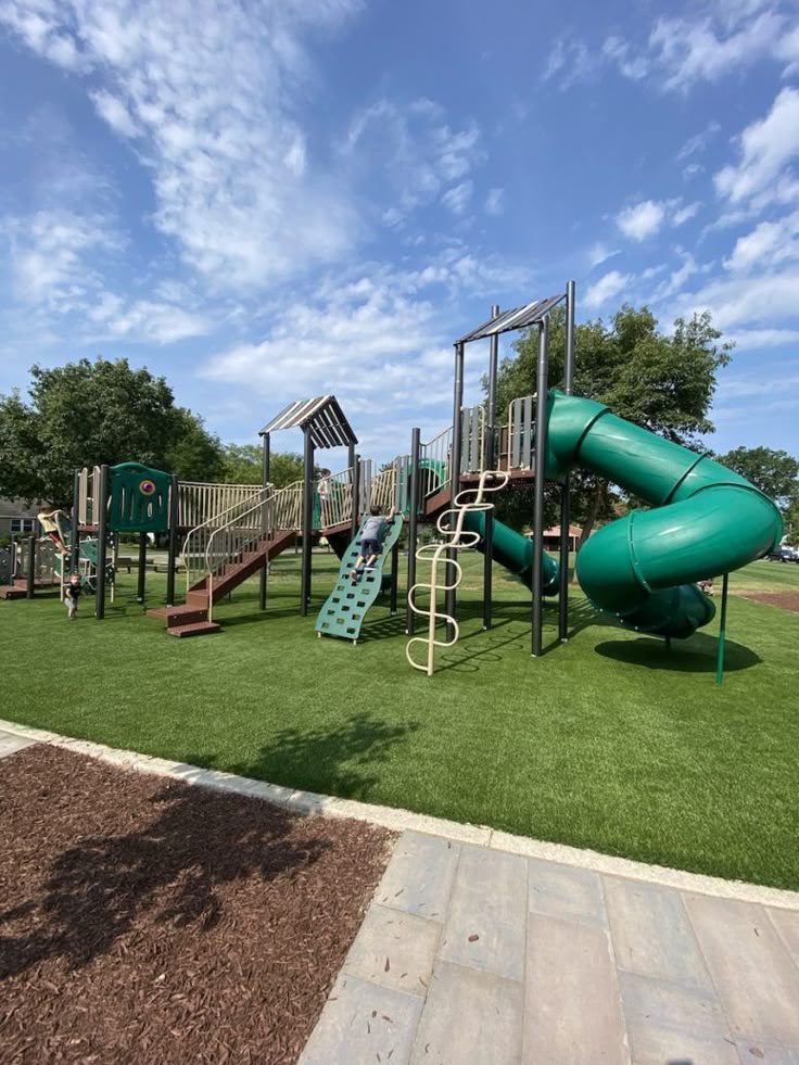 a green playground with slides and climbing equipment on artificial grass in front of a blue sky