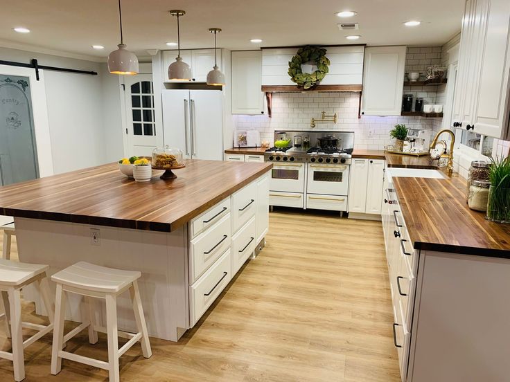 a large kitchen with white cabinets and wooden counter tops, along with bar stools