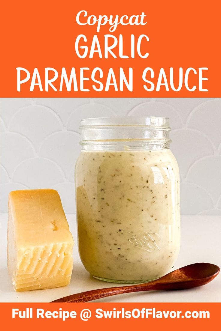 a jar filled with garlic parmesan sauce next to a wooden spoon and cheese