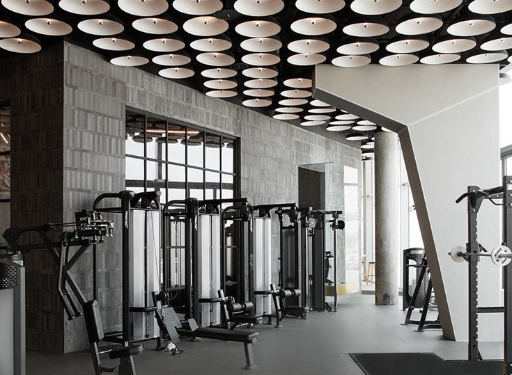 a gym with rows of exercise equipment and mirrors on the wall, along with windows