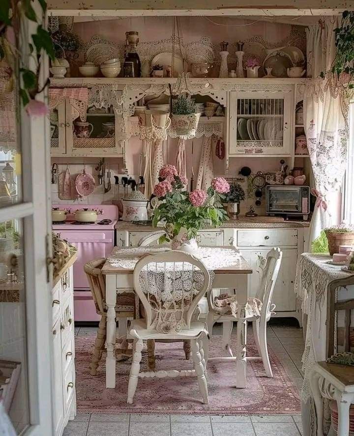 an old fashioned kitchen with white cabinets and pink flowers on the counter top, along with antique furniture