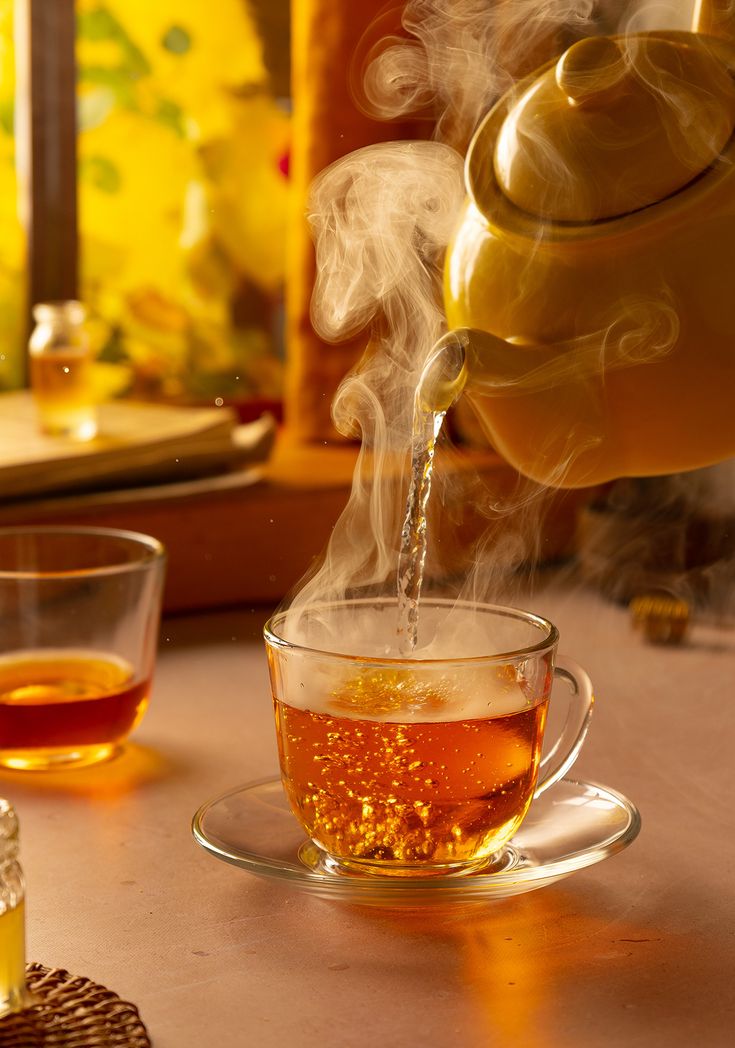 tea being poured into a glass cup with steam rising from the top, on a table