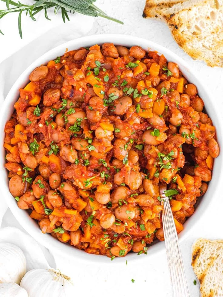 a white bowl filled with beans and parsley next to garlic bread on the side