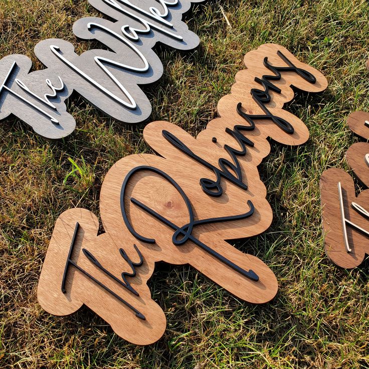 three wooden signs sitting on top of a grass covered field with the word welcome written in cursive writing