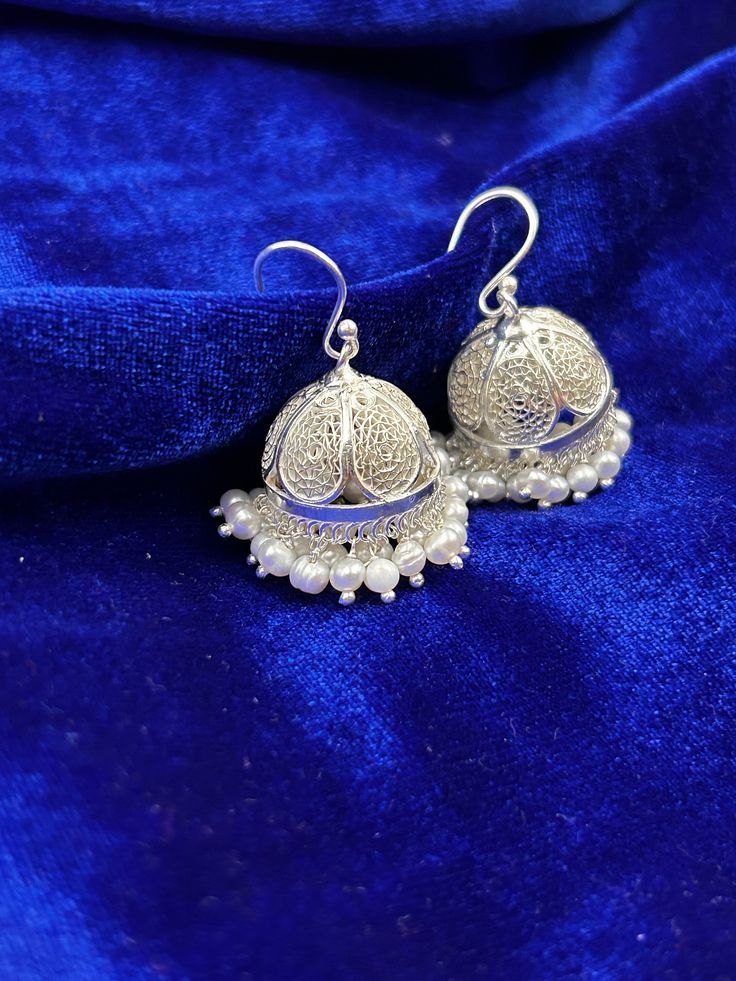 Jhumka is a masterpiece, meticulously handcrafted by skilled artisans who infuse every curve and detail with love and artistry. The sterling silver metal, known for its lustrous shine and durability, serves as the perfect canvas for intricate designs and embellishments. Silver jhumkas can go with any attire, whether ethnic or western, casual or stylish. Design : Jhumka  Material : Solid sterling silver Weight : Approximately 17 gm Contact us for more information Handmade Silver Metal Jhumkas, Handmade Silver Fusion Style Jhumkas, Handmade Silver Fusion Jhumkas, Silver Metal Fusion Jhumkas, Silver Fusion Style Metal Jhumkas, Silver Metal Fusion Style Jhumkas, Fusion Style White Bridal Earrings With Latkans, Silver Metal Bridal Earrings For Festivals, Silver Fusion Bridal Earrings With Intricate Design