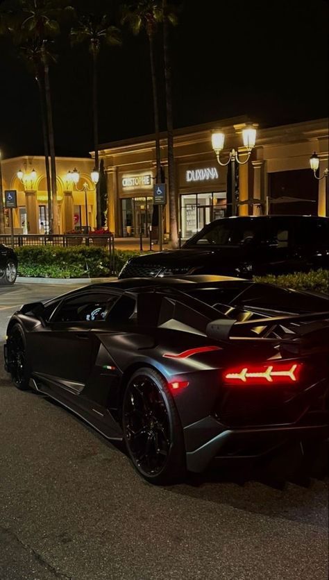 two black sports cars parked in front of a building with palm trees on the street