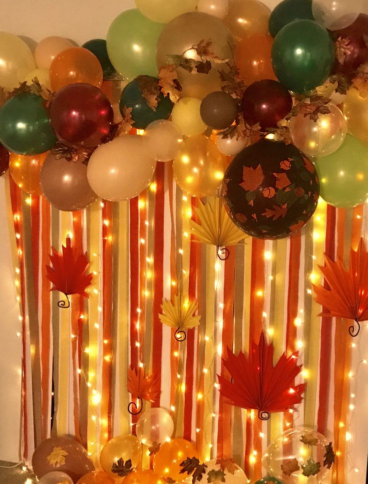 balloons and streamers are hanging from the ceiling in front of an autumn themed backdrop