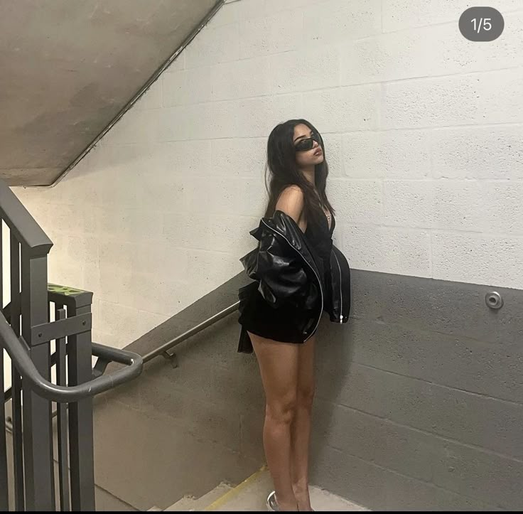 a woman in black jacket and shorts standing next to an escalator with her hand on her hip