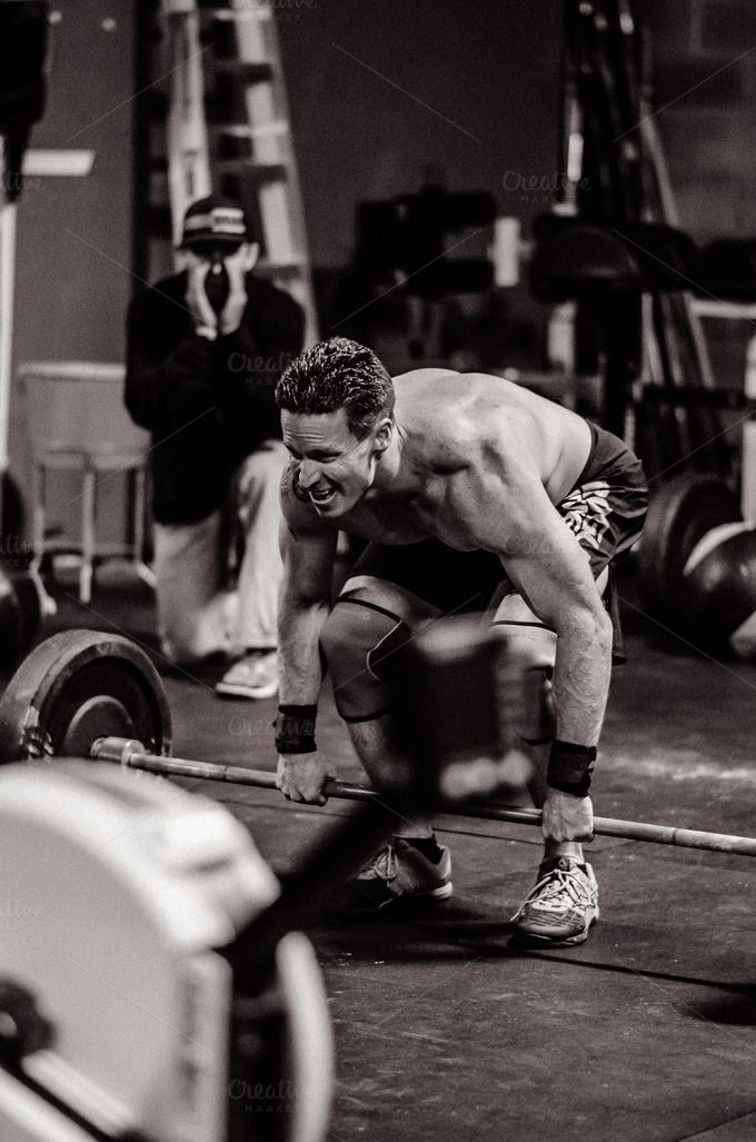 a man squatting down while holding a barbell in front of his face and looking at the ground