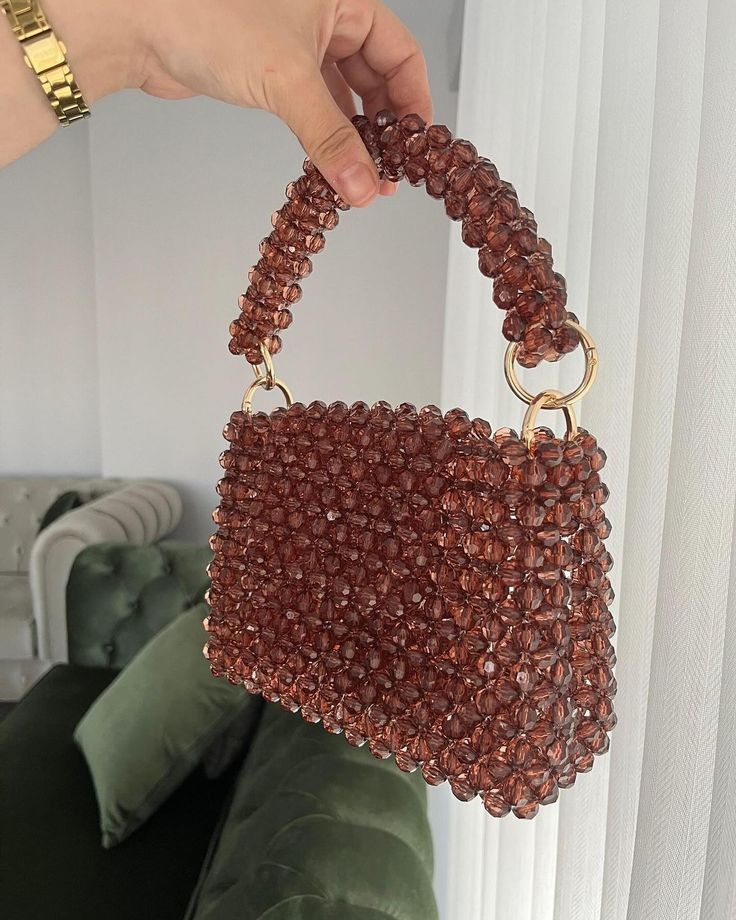 a hand holding a brown beaded purse in front of a green velvet couch with white curtains