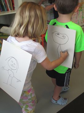 two children holding drawings in front of them