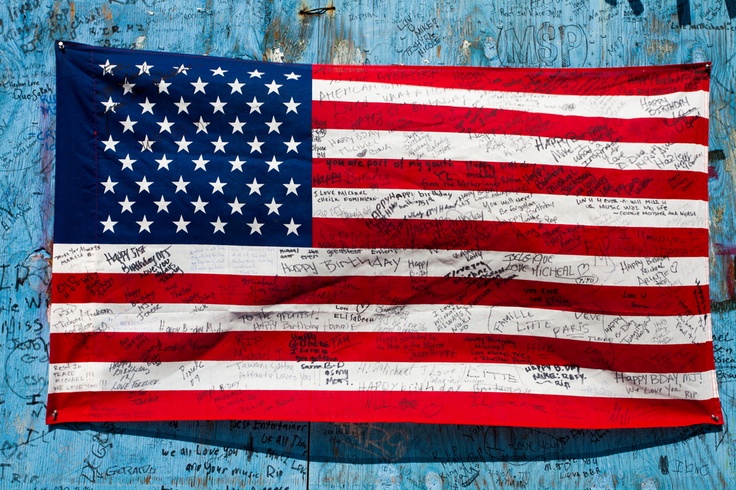 an american flag with writing on it in front of a blue wall covered in graffiti