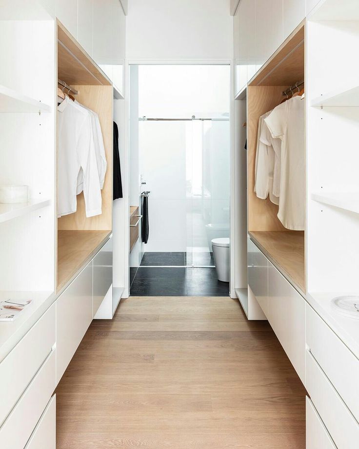 an empty walk - in closet with white cabinets and wood flooring on the walls