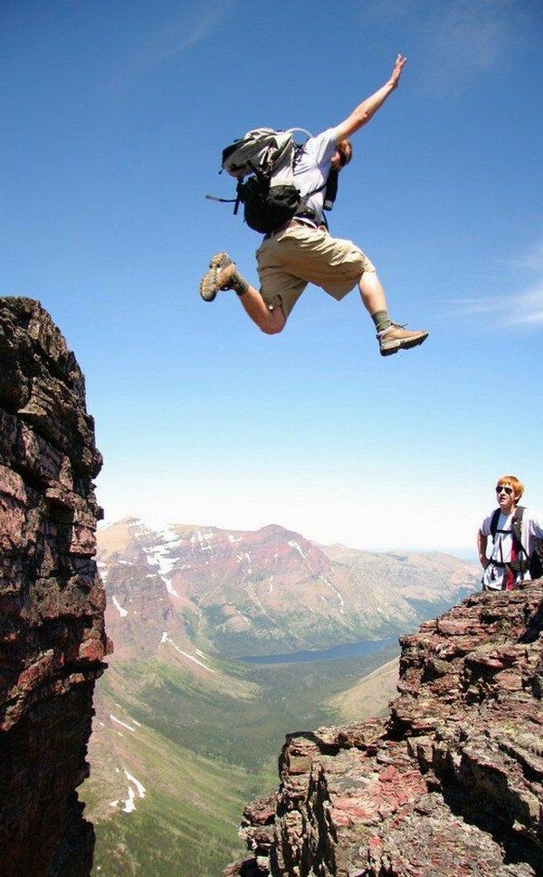 a man jumping off the side of a cliff into the air with his backpack on