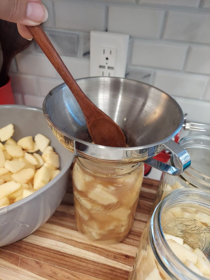 a wooden spoon in a glass jar filled with apple slices next to another bowl full of apples